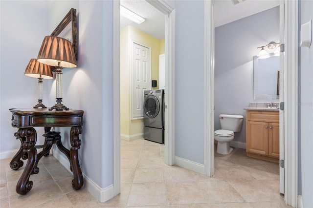 bathroom featuring toilet, washer / dryer, baseboards, and vanity