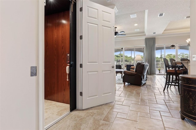 foyer entrance featuring ceiling fan, a textured ceiling, visible vents, ornamental molding, and a tray ceiling