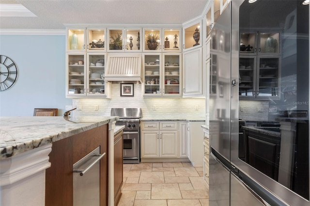 kitchen with tasteful backsplash, custom range hood, ornamental molding, light stone countertops, and refrigerator with glass door