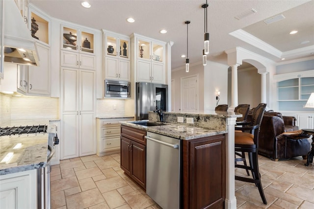 kitchen with range hood, stainless steel appliances, open floor plan, a sink, and ornate columns