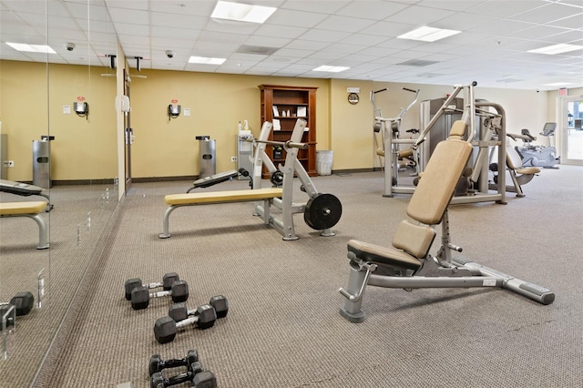 exercise room featuring a paneled ceiling and baseboards