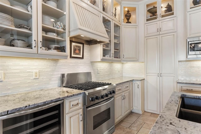 kitchen with light stone counters, beverage cooler, stainless steel appliances, backsplash, and custom exhaust hood