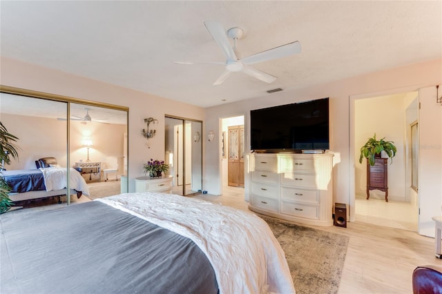 bedroom featuring multiple closets, ceiling fan, connected bathroom, and light hardwood / wood-style floors