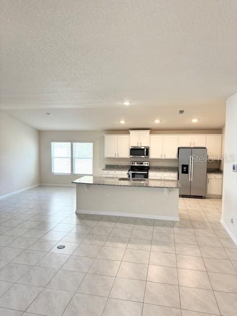 kitchen with a kitchen island with sink, appliances with stainless steel finishes, stone countertops, and white cabinets