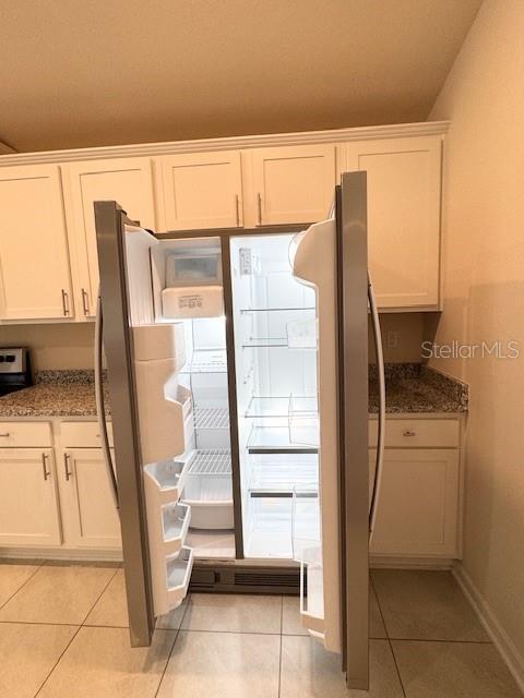 kitchen featuring light tile patterned flooring, stainless steel refrigerator, dark stone counters, and white cabinets