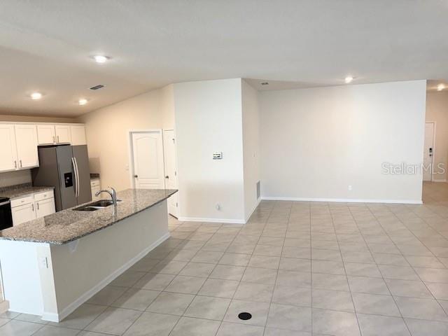 kitchen with white cabinetry, sink, stainless steel fridge, light stone countertops, and a center island with sink