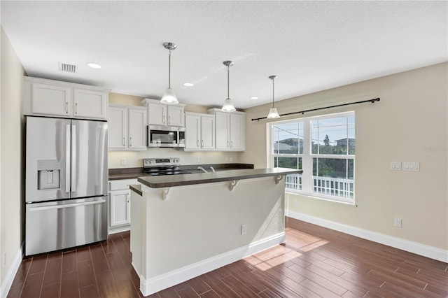 kitchen with appliances with stainless steel finishes, a breakfast bar area, white cabinets, dark hardwood / wood-style flooring, and hanging light fixtures