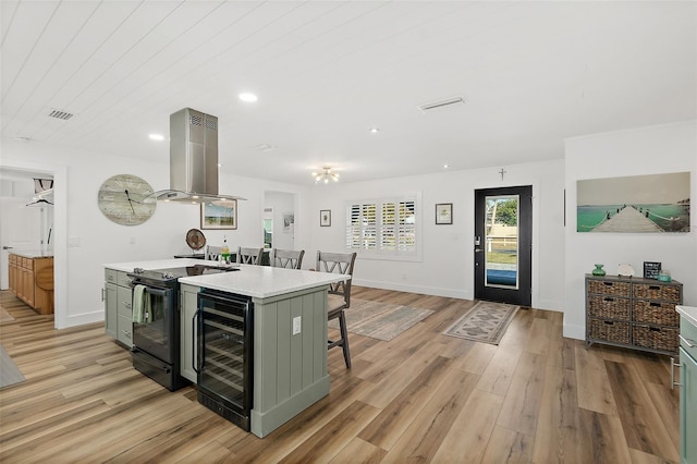 kitchen with beverage cooler, island exhaust hood, light hardwood / wood-style floors, black range with electric cooktop, and a center island with sink