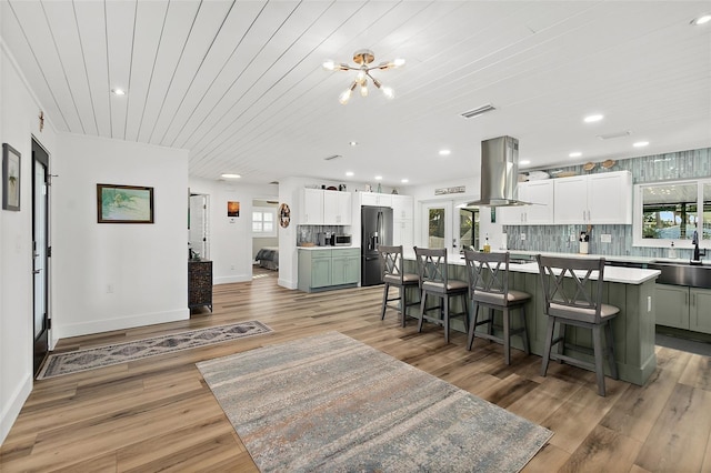 kitchen featuring plenty of natural light, a kitchen island, island exhaust hood, black refrigerator with ice dispenser, and a sink