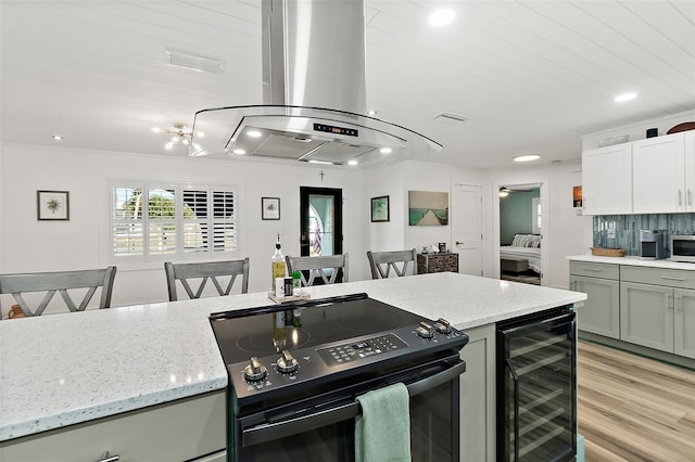 kitchen with island exhaust hood, visible vents, light wood-style floors, beverage cooler, and black range with electric cooktop