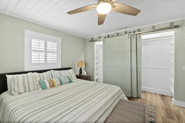 bedroom with light hardwood / wood-style flooring, a barn door, and ceiling fan