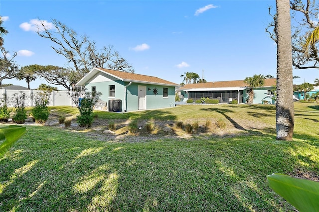 rear view of house featuring a yard, fence, a sunroom, and stucco siding