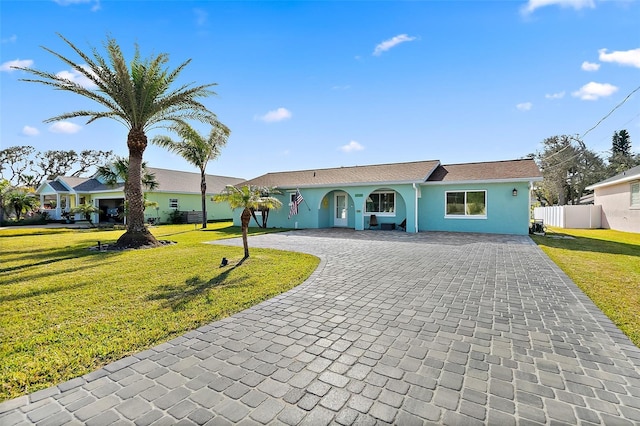 ranch-style house with a front yard, decorative driveway, fence, and stucco siding