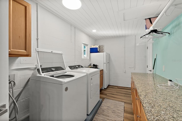 laundry area with concrete block wall, cabinet space, wood ceiling, wood finished floors, and washing machine and dryer