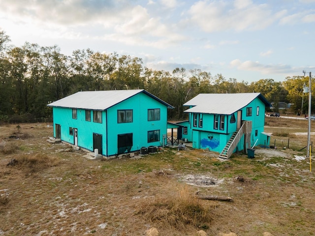 rear view of property with stairs and view of scattered trees