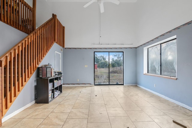living room featuring a ceiling fan, a high ceiling, tile patterned floors, stairs, and baseboards