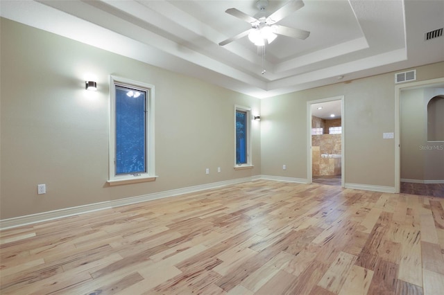 spare room with light wood finished floors, a raised ceiling, visible vents, and baseboards