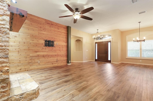 unfurnished living room featuring visible vents, wood walls, wood finished floors, baseboards, and ceiling fan with notable chandelier