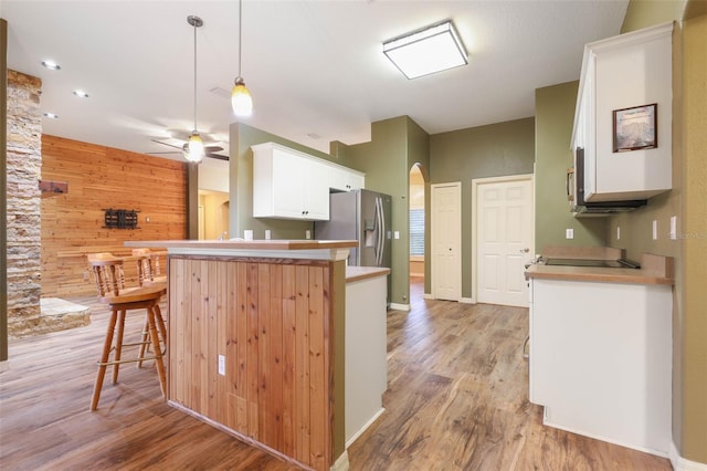 kitchen featuring arched walkways, stainless steel fridge with ice dispenser, a breakfast bar area, decorative light fixtures, and a peninsula