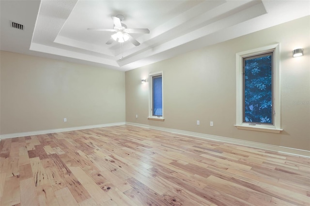 spare room featuring a tray ceiling, visible vents, light wood-style floors, ceiling fan, and baseboards