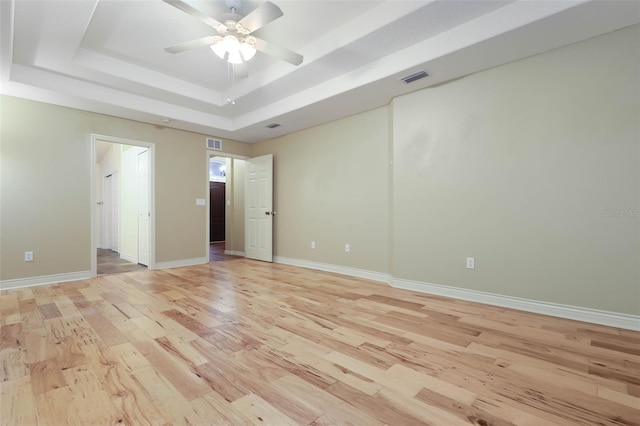 unfurnished room with a raised ceiling, visible vents, light wood-style flooring, and baseboards