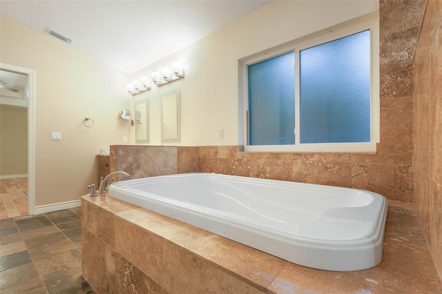 bathroom with visible vents, a textured ceiling, vanity, and a bath