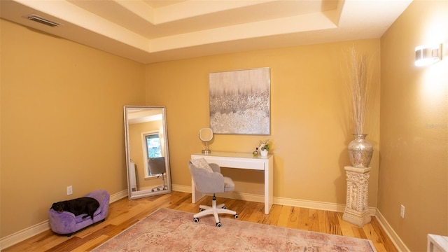 office with a tray ceiling, visible vents, baseboards, and wood finished floors