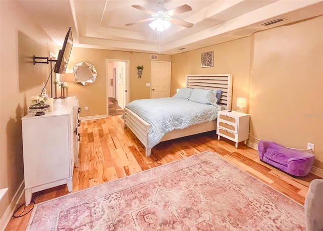 bedroom featuring light wood-style floors, a tray ceiling, visible vents, and baseboards