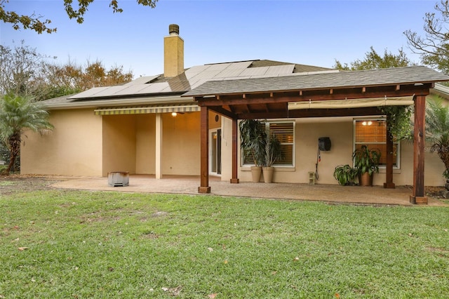 back of house with stucco siding, roof mounted solar panels, a chimney, and a patio