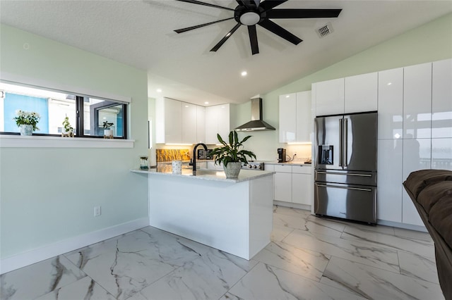 kitchen featuring high end fridge, kitchen peninsula, white cabinets, and wall chimney exhaust hood