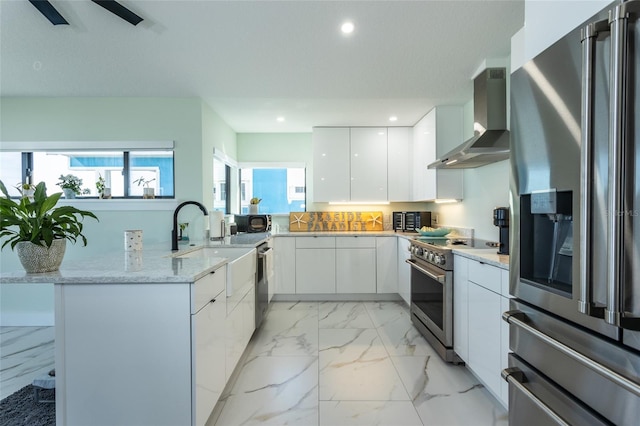 kitchen with wall chimney exhaust hood, high end appliances, kitchen peninsula, a healthy amount of sunlight, and white cabinets