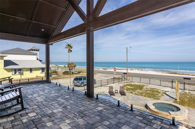 view of patio featuring a water view, an in ground hot tub, and a view of the beach