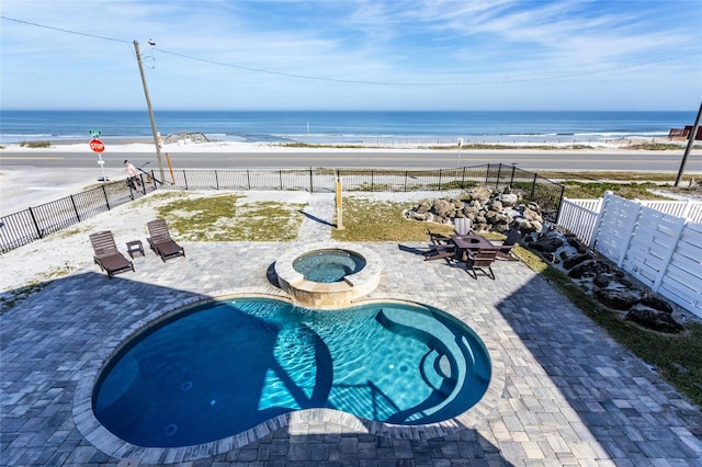 view of swimming pool featuring a water view, a beach view, and an in ground hot tub