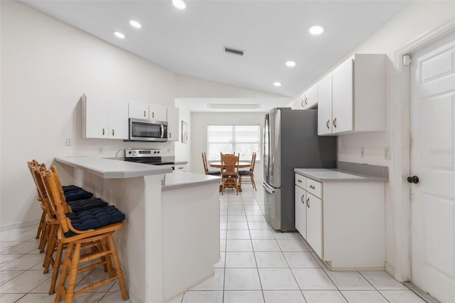 kitchen with lofted ceiling, a breakfast bar area, appliances with stainless steel finishes, kitchen peninsula, and white cabinets