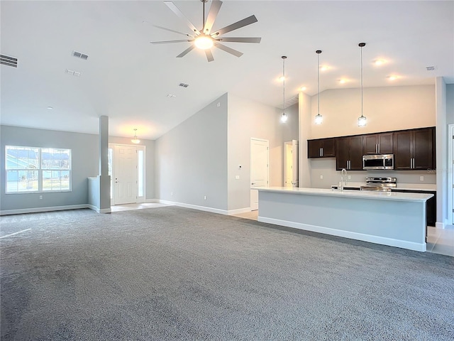 kitchen with high vaulted ceiling, dark brown cabinets, a center island with sink, pendant lighting, and stainless steel appliances