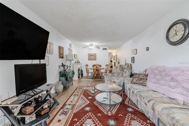 living room with a textured ceiling, ceiling fan, and light wood-type flooring