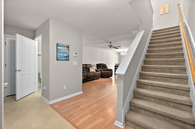 staircase with wood-type flooring, ceiling fan with notable chandelier, and a textured ceiling