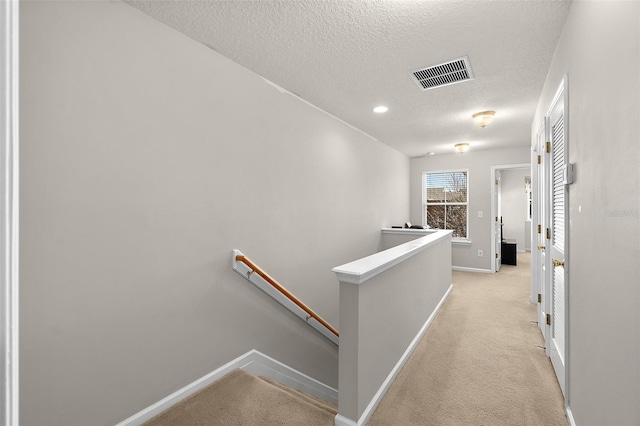 corridor featuring light carpet and a textured ceiling