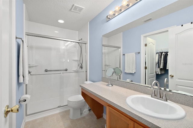 bathroom with vanity, toilet, a shower with shower door, and a textured ceiling