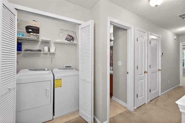 laundry room with washing machine and dryer, light colored carpet, and a textured ceiling