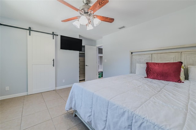 bedroom with ceiling fan, a barn door, and light tile patterned floors