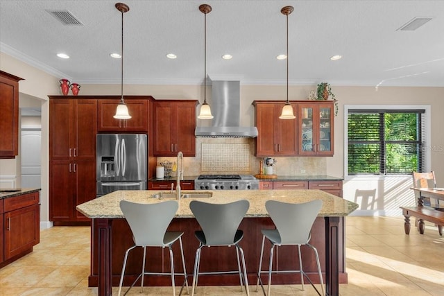 kitchen with an island with sink, wall chimney exhaust hood, sink, and stainless steel fridge with ice dispenser