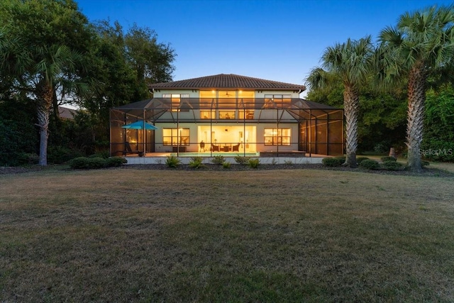 back house at dusk with a yard, a lanai, and a balcony