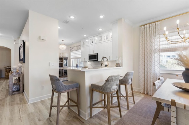 kitchen featuring light hardwood / wood-style flooring, backsplash, white cabinets, kitchen peninsula, and a chandelier