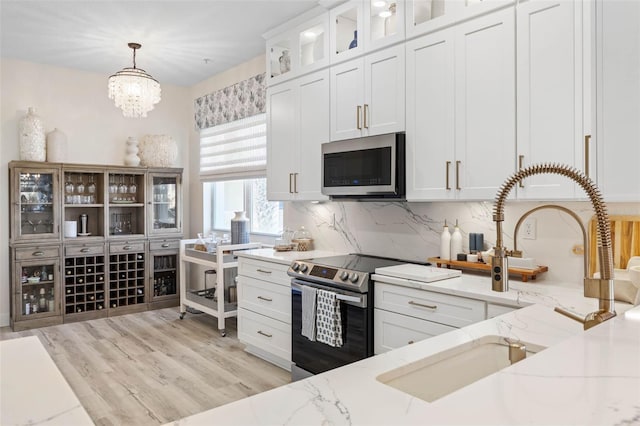 kitchen with appliances with stainless steel finishes, pendant lighting, white cabinets, and light stone counters