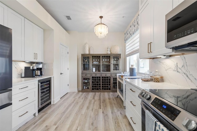 kitchen featuring stainless steel appliances, light hardwood / wood-style floors, white cabinets, decorative light fixtures, and beverage cooler