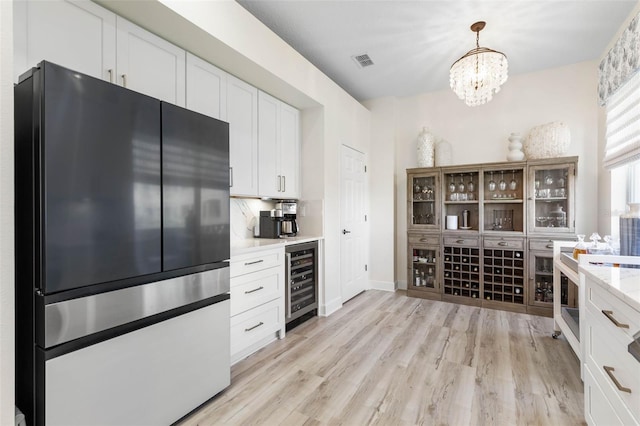 kitchen with stainless steel fridge, wine cooler, white cabinets, decorative light fixtures, and light wood-type flooring