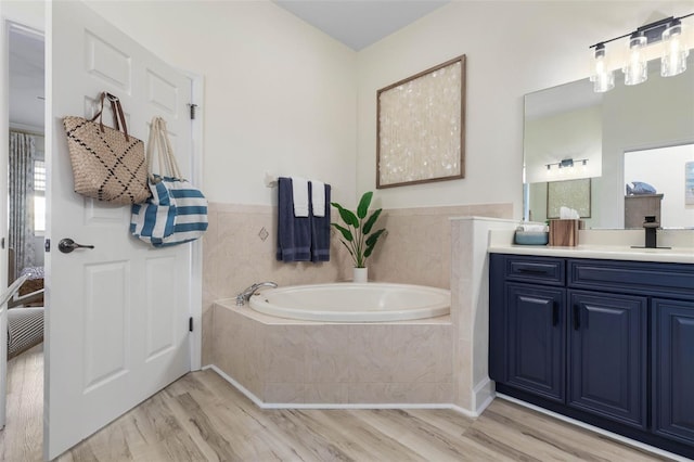 bathroom featuring a relaxing tiled tub, vanity, and hardwood / wood-style floors