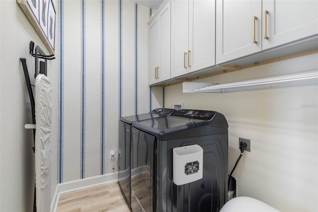 washroom featuring cabinets, washing machine and clothes dryer, and light hardwood / wood-style flooring