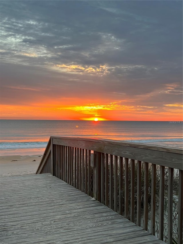 deck at dusk featuring a water view and a beach view